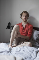 Junger Mann sitzt zu Hause auf dem Bett - FSIF00212