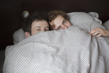 Hochwinkliges Porträt eines jungen schwulen Paares, das im Bett durch das Laken schaut - FSIF00214