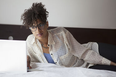 Junge Frau mit Laptop auf dem Bett zu Hause - FSIF00216