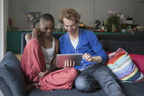 Lächelnde Freunde, die gemeinsam auf dem Sofa zu Hause ein digitales Tablet benutzen - FSIF00228