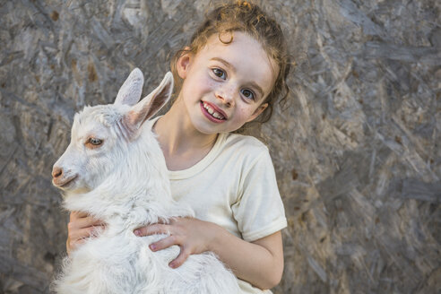 Porträt eines niedlichen Mädchens, das eine kleine Ziege im Freien hält - FSIF00234