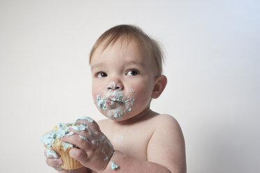 Nettes Baby mit unordentlichem Mund schaut weg, während er ein Törtchen vor weißem Hintergrund hält - FSIF00250
