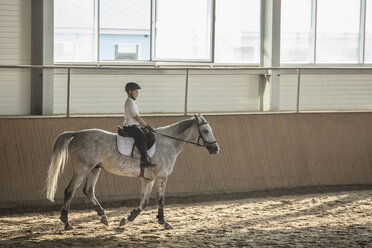 Seitenansicht eines Jungen, der auf einem Pferd im Trainingsstall sitzt - FSIF00258