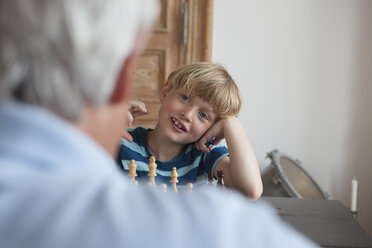 Happy boy playing chess with grandfather at home - FSIF00266