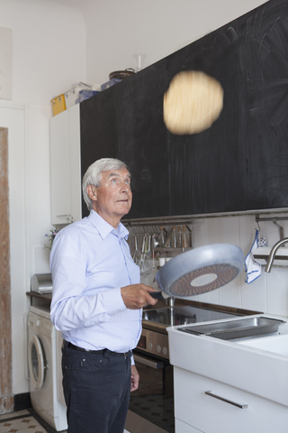 Älterer Mann wirft Pfannkuchen auf Bratpfanne in Küche zu Hause, lizenzfreies Stockfoto