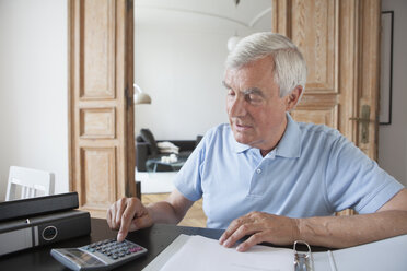 Ein älterer Mann rechnet am Tisch mit einem Taschenrechner die Finanzen seines Hauses aus - FSIF00272