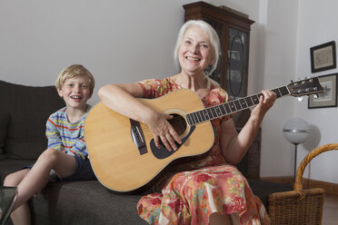 Porträt eines Jungen, der mit seiner Großmutter zu Hause auf dem Sofa sitzt und Gitarre spielt - FSIF00276