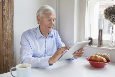 Älterer Mann benutzt digitales Tablet am Frühstückstisch - FSIF00281