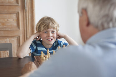 Happy grandson playing chess with grandfather at home - FSIF00283