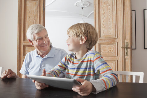 Happy senior man looking at grandson with digital tablet at home - FSIF00286