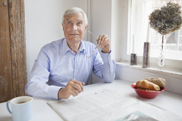 Nachdenklicher älterer Mann, der am Frühstückstisch ein Glas in der Hand hält und wegschaut - FSIF00287