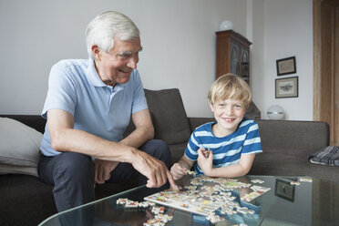 Porträt eines glücklichen Jungen, der mit seinem Großvater im heimischen Wohnzimmer ein Puzzle löst - FSIF00288