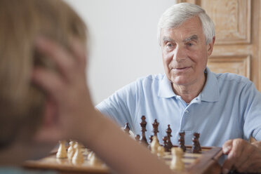 Senior man playing chess with grandson at home - FSIF00289