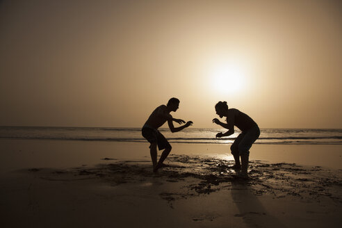 Volle Länge der Silhouette männliche Freunde spielen am Strand bei Sonnenuntergang - FSIF00314