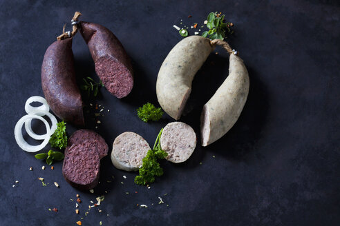 Sliced liver sausages and blood sausages, onion rings, parsley and herbs on dark ground - CSF28903