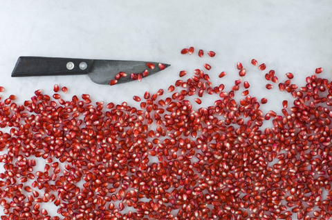 Pomegranate seeds and knife on white marble stock photo