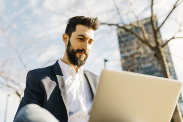 Businessman using laptop outside office building - JRFF01538