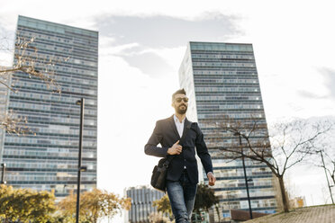 Businessman wearing sunglasses walking outside office building - JRFF01542