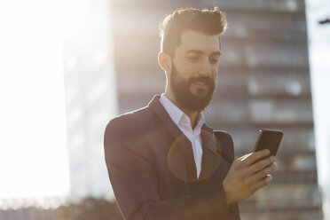 Businessman using cell phone outside office building - JRFF01544