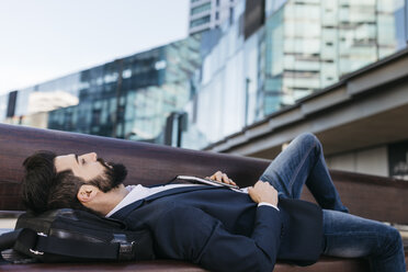 Businessman lying on bench outside office building - JRFF01545