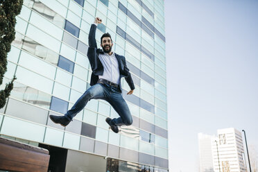 Businessman jumping outside office building - JRFF01548
