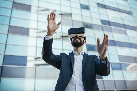 Geschäftsmann mit Virtual-Reality-Brille vor einem Bürogebäude, lizenzfreies Stockfoto