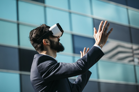 Geschäftsmann mit Virtual-Reality-Brille vor einem Bürogebäude, lizenzfreies Stockfoto