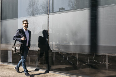 Businessman wearing sunglasses walking along building - JRFF01552
