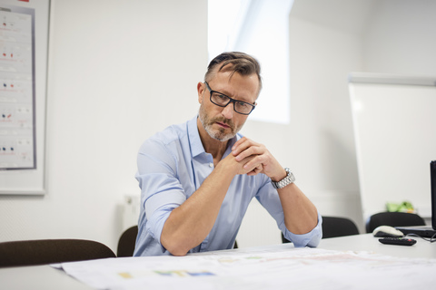 Mature businessman looking at plan on desk in office stock photo
