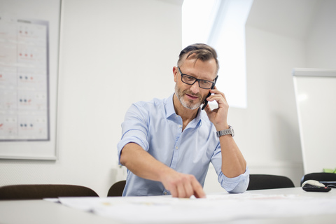 Älterer Geschäftsmann telefoniert am Schreibtisch im Büro, lizenzfreies Stockfoto