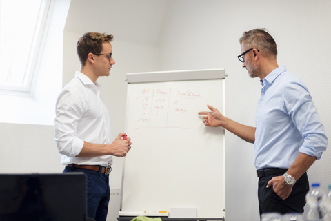 Two businessmen discussing at flip chart in office stock photo