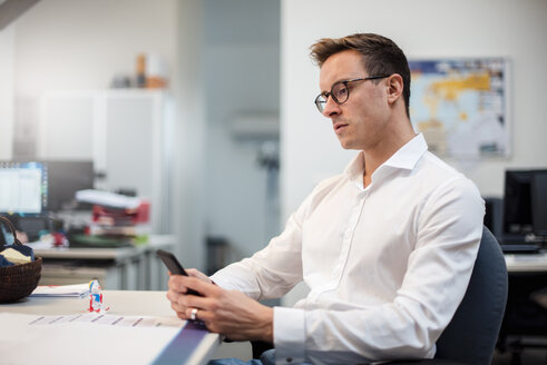 Junger Geschäftsmann benutzt Mobiltelefon am Schreibtisch im Büro - DIGF03315