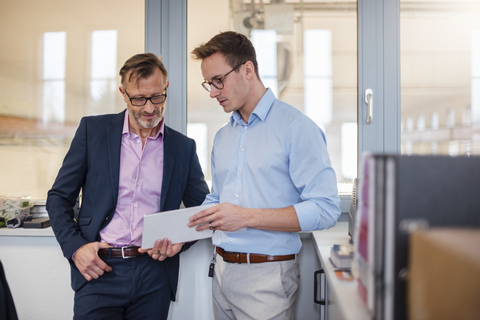 Two businessmen sharing tablet in office stock photo