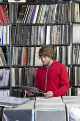 Ein junger Mann betrachtet eine Schallplatte in einem Plattenladen - FSIF00360