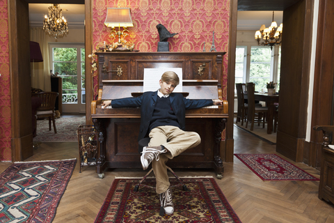 A boy with a cool attitude posing at an old-fashioned upright piano stock photo