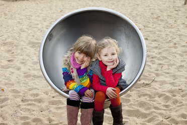 Two girls sitting on spherical metal chair in park - FSIF00415