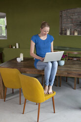 Eine Frau sitzt an ihrem Esstisch und benutzt einen Laptop - FSIF00438