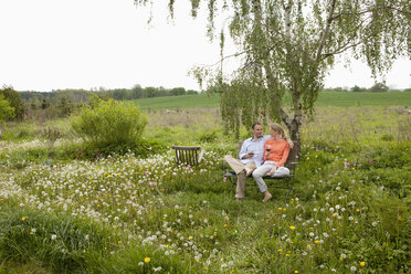 Ein Paar unterhält sich und genießt ein Glas Wein auf einer Bank in seinem Garten - FSIF00439