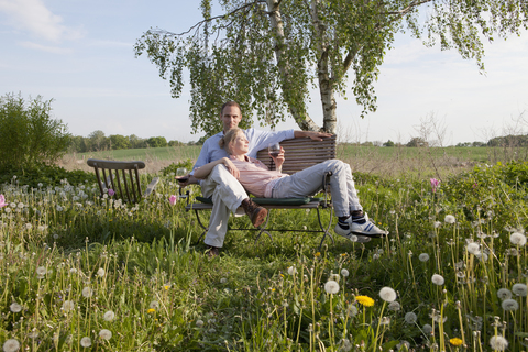 Ein Paar genießt die Sonne und den Wein auf einer Bank in seinem Garten, lizenzfreies Stockfoto