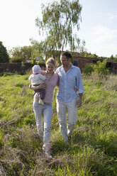 Ein Mann und eine Frau, die ein Baby halten, gehen hinter ihrem Landhaus spazieren - FSIF00441
