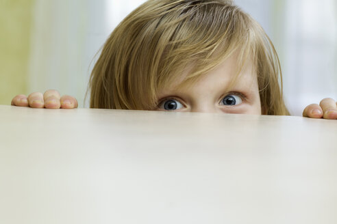 A mischievous girl peeking over the top of a table - FSIF00467