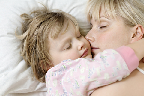 A mother and her young daughter sleeping a bed side by side stock photo