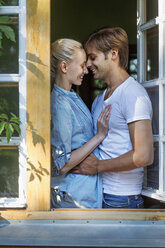 Ein fröhliches Paar umarmt sich vor einem offenen Fenster - FSIF00529