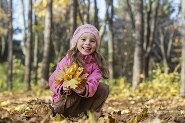 Ein fröhliches Mädchen sammelt Herbstblätter in einem Waldgebiet auf - FSIF00544