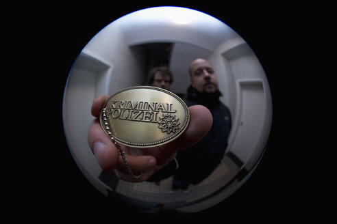 Zwei Kriminalbeamte zeigen einem Guckloch ein Abzeichen der Kriminalpolizei - FSIF00549