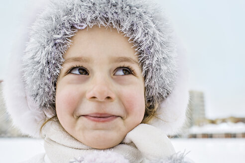 A mischievously smiling young girl wearing a fur hat outdoors in winter - FSIF00603