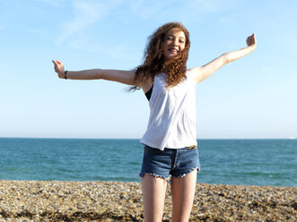 Ein fröhliches Teenager-Mädchen, das am Strand steht und die Arme vor Freude hebt - FSIF00616