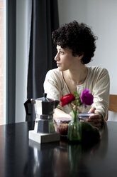 Eine Frau sitzt an einem Tisch und schaut nachdenklich aus dem Fenster - FSIF00624