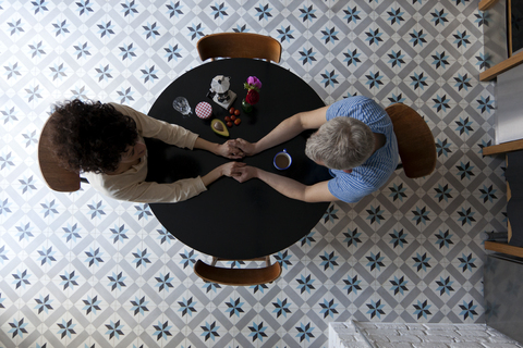 A mixed age couple holding hands at the breakfast table, directly above stock photo