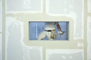 A house painter holding a trowel, seen through window hole in a newly constructed wall - FSIF00653